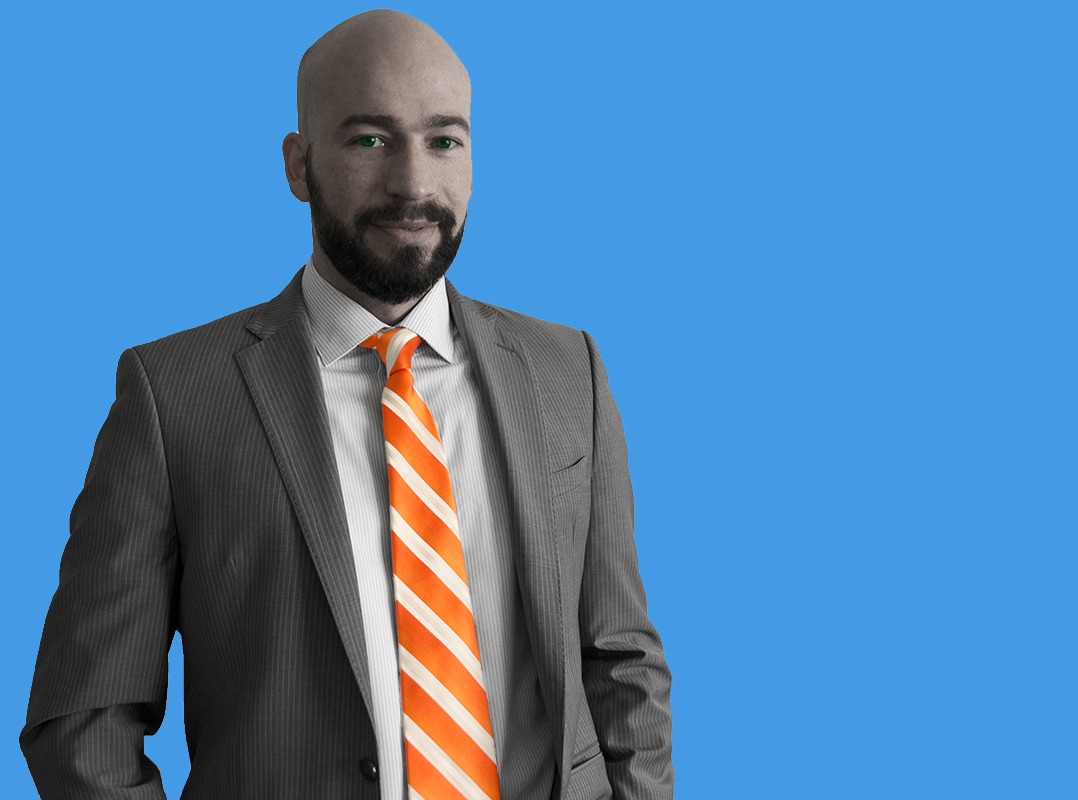 David Dubé in a grey suit and orange striped tie against a blue background.